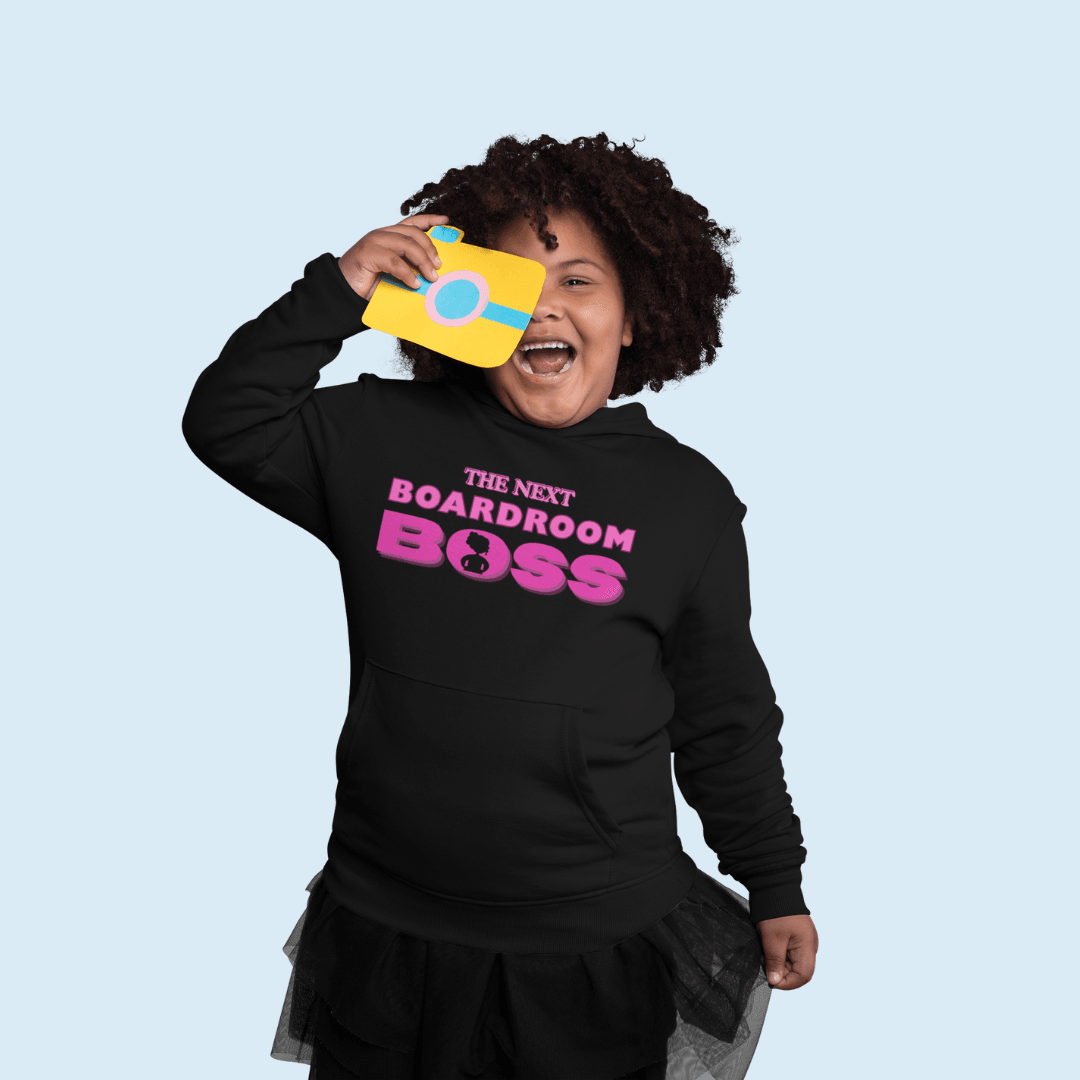 Young Black girl with fake camera wearing The Next Boardroom Boss Hoodie from TL Johnson’s Mini Monarchs Apparel; motivational fashion for future leaders. Featuring Pink typography