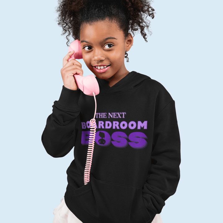 Young Black girl with a fake phone wearing The Next Boardroom Boss Hoodie from TL Johnson’s Mini Monarchs Apparel; motivational fashion for future leaders. Featuring purple typography