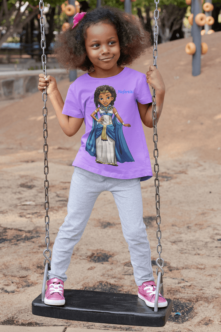 Young Black girl smiling on a playground swing wearing a purple Nefertiti T-shirt from TL Johnson’s Mini Monarchs collection, celebrating African royalty and Black heritage.