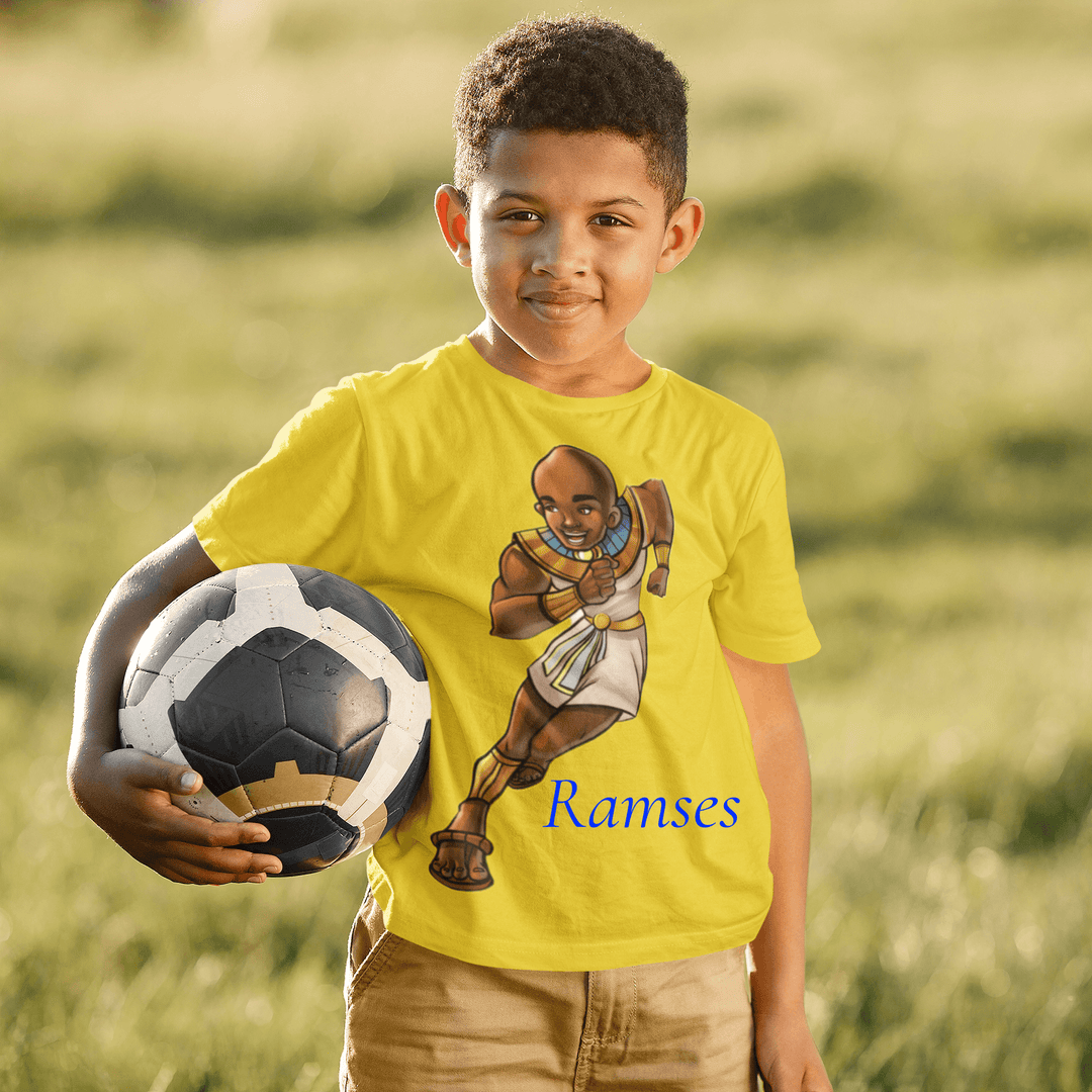 Boy, holding a soccer ball, while wearing Gold Ramses T-shirt from TL Johnson’s Mini Monarchs collection celebrating intelligence and royal leadership. 