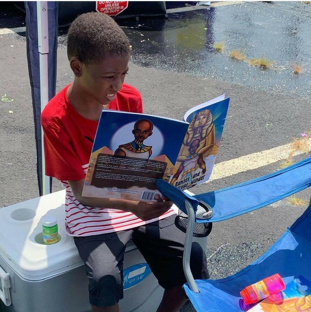 Youg kid outside reading Ramses & The Great wonder sitting ont a gray cooler.