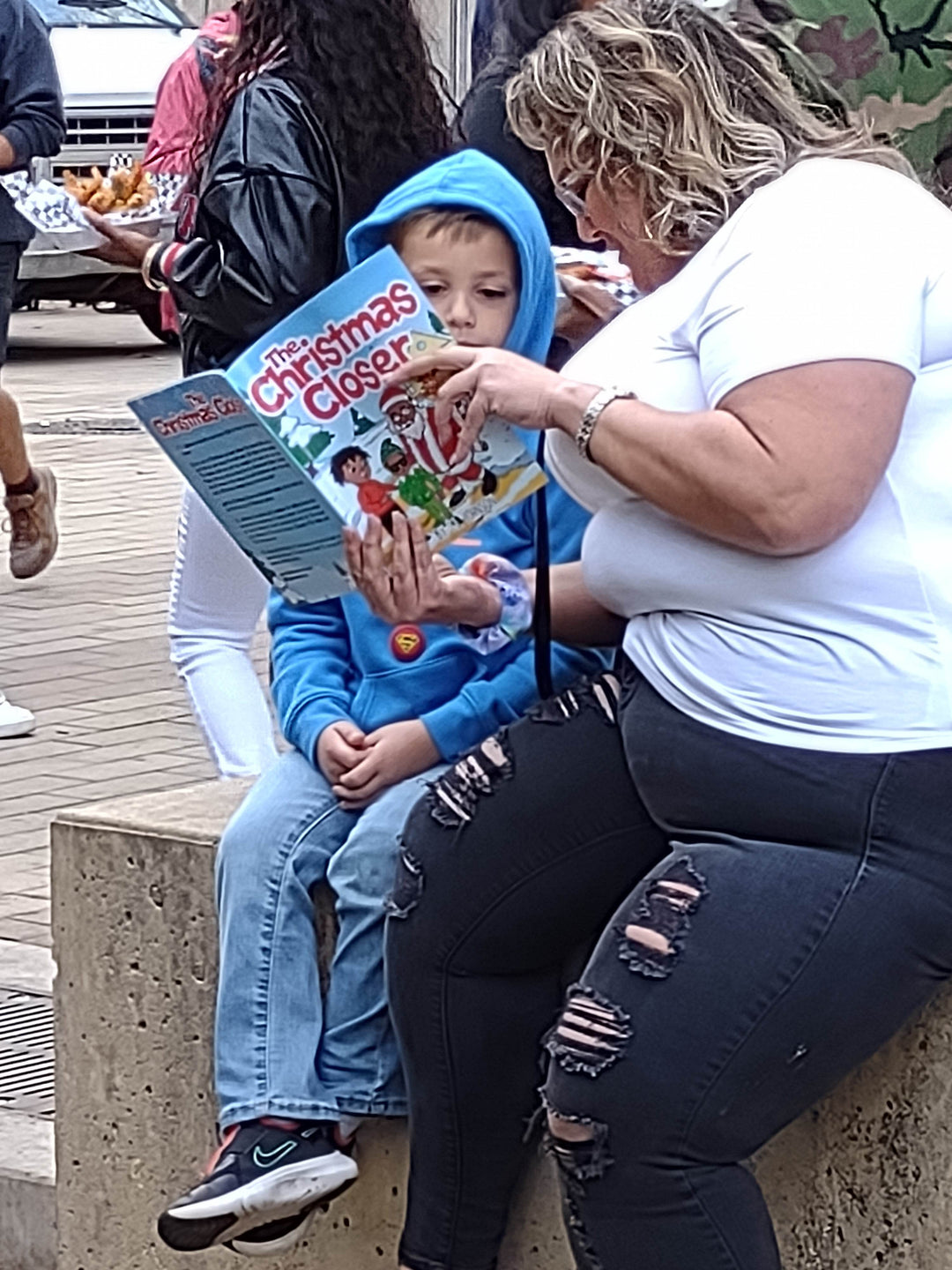 A woman reading The Christmas Closer to a boy in a blue hoodie